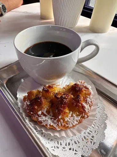 A cup of black coffee beside a coconut topped pastry