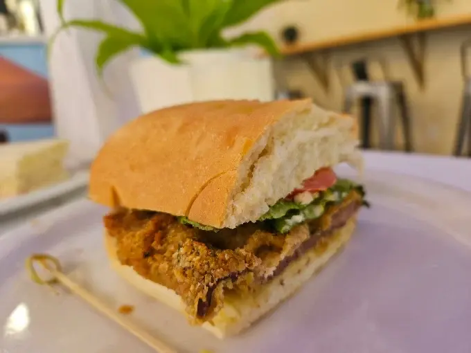 A milanesa sandwich on the counter with the dining room behind it