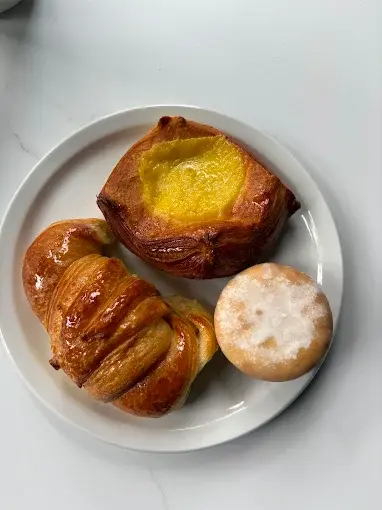 A plate with a medialuna, a custard factura and a powdered pastry